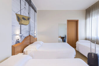 Hotel room at B&B Hotel Pescara with three white beds, wooden headboards, a large boat wall mural, and a suitcase by the bed