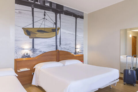 Hotel room at B&B Hotel Pescara with double bed, single bed, large wall photo of a yellow boat, suitcase, and full-length mirror