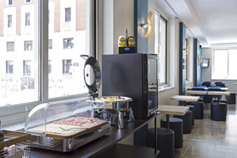 Breakfast buffet area with sliced ham, cheese, a chafing dish, condiments, and seating in B&B Hotel Pescara