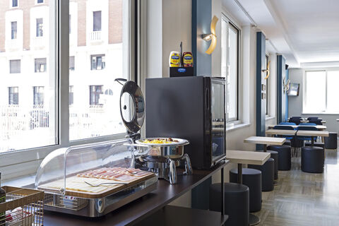 Breakfast buffet area with sliced ham, cheese, a chafing dish, condiments, and seating in B&B Hotel Pescara