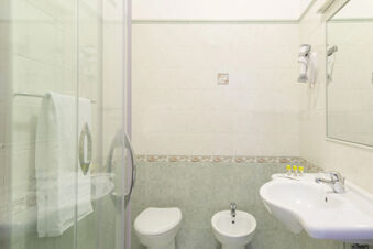 Bathroom interior at B&B Hotel Pescara with white toilet, bidet, sink, mirror, hairdryer, and glass shower door with towel rack