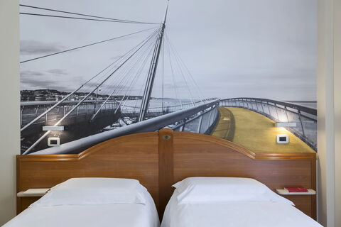 Two white beds with wooden headboard are set against a wall mural of a bridge in a room at B&B Hotel Pescara