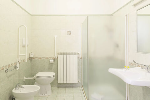 Modern bathroom with toilet, bidet, frosted glass shower, white sink, and safety bars at B&B Hotel Pescara
