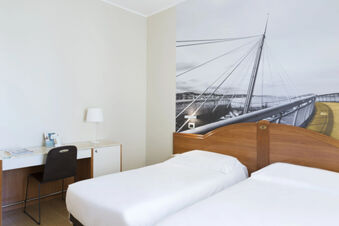 Two single beds with white linens, wooden headboards, a desk with a lamp and chair, and bridge mural at B&B Hotel Pescara