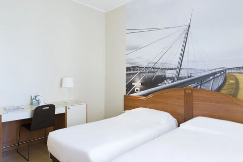 Two single beds with white linens, wooden headboards, a desk with a lamp and chair, and bridge mural at B&B Hotel Pescara