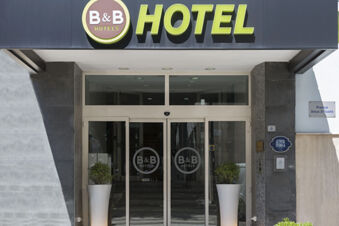 Entrance of B&B Hotel Pescara with automatic glass doors displaying the B&B Hotels logo and two tall white planters