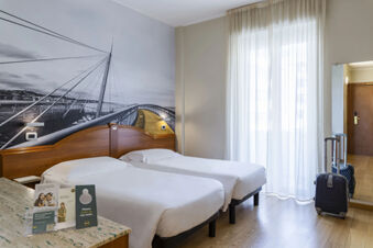 Twin beds with white linens, a wall mural of a bridge, suitcase, full-length mirror, and sheer curtains at B&B Hotel Pescara