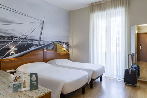 Twin beds with white linens, a wall mural of a bridge, suitcase, full-length mirror, and sheer curtains at B&B Hotel Pescara