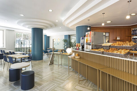 Breakfast area at B&B Hotel Pescara with baskets of bread and pastries on the counter near blue pillars and seating tables