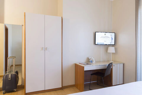 Wardrobe, full-length mirror with suitcase reflection, a desk with chair, lamp, and mounted TV screen in B&B Hotel Pescara room