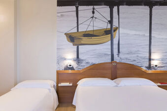 Bedroom at B&B Hotel Pescara with two beds, wooden headboard, white bedding, and a large wall mural of a yellow boat over water