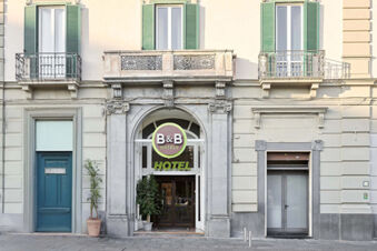 Entrance of B&B Hotel Napoli with large stone archway, green shutters above, and two potted plants beside the doors