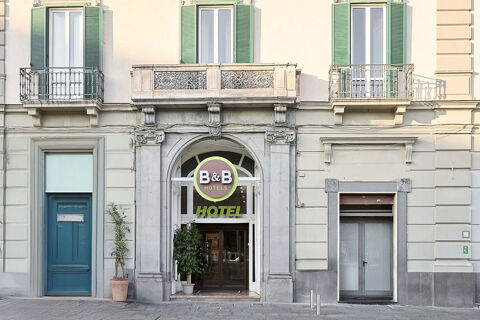 Entrance of B&B Hotel Napoli with large stone archway, green shutters above, and two potted plants beside the doors