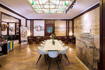 Dining area with white chairs around a table, brown stools, framed pictures, and a decorative ceiling at B&B Hotel Napoli
