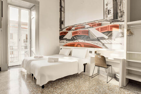 Two single beds with white linens and towels are arranged next to a window and a desk with a chair at B&B Hotel Napoli