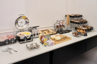 Breakfast buffet with sliced bread, cold cuts, scrambled eggs, condiments, pastries, and jam dispensers at B&B Hotel Napoli