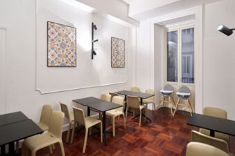 Dining area at B&B Hotel Napoli with black tables, beige chairs, two high chairs, wooden floor, and decorative wall art