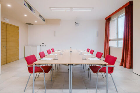 Conference room with red chairs around two tables, water glasses, notepads, a wooden door, and window at B&B Hotel Reggio Emilia Remilia
