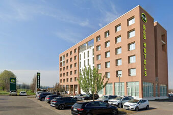 View of the B&B Hotel Reggio Emilia Remilia building with multiple windows and parked cars in the lot under a blue sky