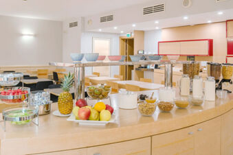 Breakfast buffet setup with fruits, cereals, milk, and bowls on a wooden counter at B&B Hotel Reggio Emilia Remilia