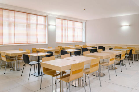 Dining area with light wooden tables and chairs, large windows with orange striped curtains at B&B Hotel Reggio Emilia Remilia
