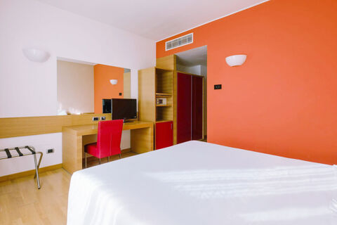 Hotel room at B&B Hotel Reggio Emilia Remilia with an orange wall, white bed, wooden desk, red chair, and TV on the desk