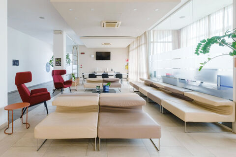 Bright hotel lounge area at B&B Hotel Reggio Emilia Remilia with cream sofas, red chairs, tables, and a wall TV