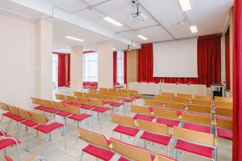 Conference room with rows of wooden chairs with red cushions, a projector, and a screen at B&B Hotel Reggio Emilia Remilia