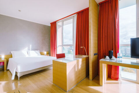 A bright hotel room at B&B Hotel Reggio Emilia Remilia with large windows, red curtains, a double bed, and modern wooden furniture