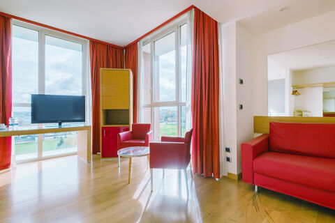 A bright hotel room at B&B Hotel Reggio Emilia Remilia with large windows, red chairs, sofa, TV, and wooden floor