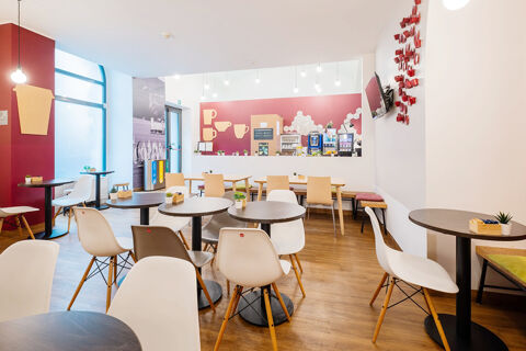 Modern dining area of B&B Hotel Trieste with white and beige chairs, round black tables, wooden floors, and beverage machines