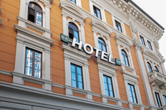 Orange and white classical building facade with multiple windows and a B&B Hotel Trieste sign in bold letters