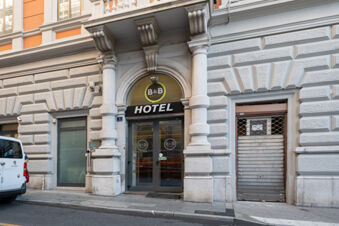 Main entrance of B&B Hotel Trieste with large archway, glass doors, stone columns, and a white Peugeot van parked nearby