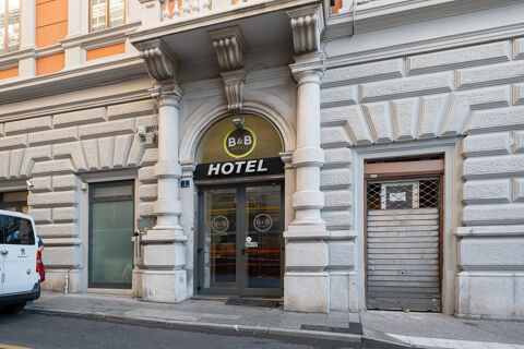 Main entrance of B&B Hotel Trieste with large archway, glass doors, stone columns, and a white Peugeot van parked nearby