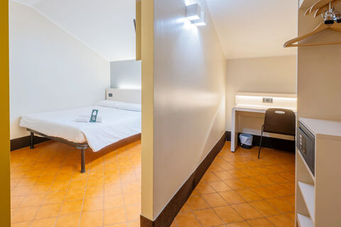 Small hotel room at B&B Hotel Trieste with tiled floors, a bed, desk, chair, and a safe on the right side