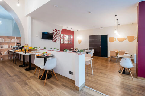 Dining area with multiple tables and chairs, wall decorations, buffet setup with food, and TV at B&B Hotel Trieste