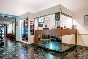 Modern reception desk with wooden panel, mirrored base, drink coolers, and digital screens inside B&B Hotel Trieste lobby