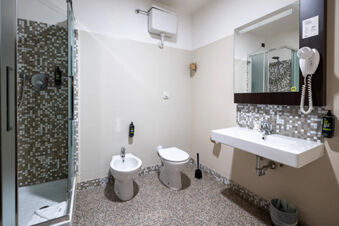 Bathroom interior at B&B Hotel Trieste with shower, bidet, toilet, wall-mounted sink, large mirror, and hairdryer unit on the wall