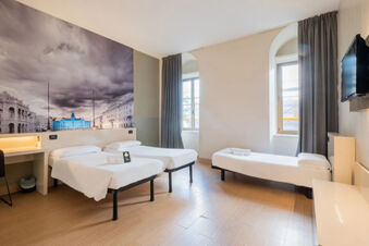 Hotel room at B&B Hotel Trieste featuring two single beds, a single bed, a wall-mounted TV, and a large cityscape mural