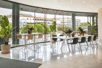 Modern seating area with tables, chairs, large windows, potted plants, and outdoor view inside B&B Hotel Latina