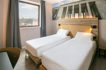 Two single beds with white linens and wooden headboard beneath a black and white wall photo in B&B Hotel Latina room