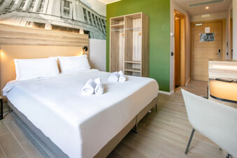 B&B Hotel Latina guest room with a neatly made double bed, white linens, wooden wardrobe, green accent wall, and desk area