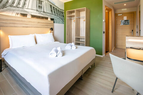 B&B Hotel Latina guest room with a neatly made double bed, white linens, wooden wardrobe, green accent wall, and desk area