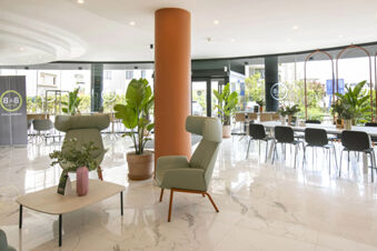Lobby seating area of B&B Hotel Latina featuring modern chairs, potted plants, marble floor, and large windows with outdoor view