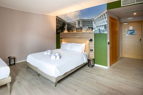 Hotel room at B&B Hotel Latina with a large bed, white linens, rolled towels, wood flooring, and a black and white wall mural