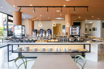 Breakfast buffet setup with coffee machines, pastries, cereal dispensers, and plates displayed in B&B Hotel Latina dining area