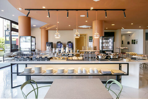 Breakfast buffet setup with coffee machines, pastries, cereal dispensers, and plates displayed in B&B Hotel Latina dining area