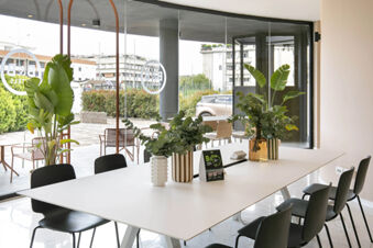 Bright meeting room with black chairs, a white table, plants in vases, and glass walls at B&B Hotel Latina