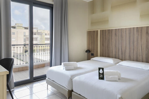 Two neatly made white beds with folded towels and a "Do Not Disturb" sign in a bright room at B&B Hotel Pomezia Cortese