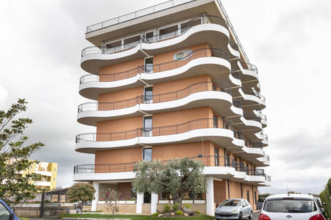 Exterior view of B&B Hotel Pomezia Cortese showing curved balconies, brick facade, parked cars, and surrounding trees and plants